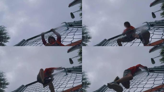 一个聪明的男孩爬过儿童游乐场的篱笆。
