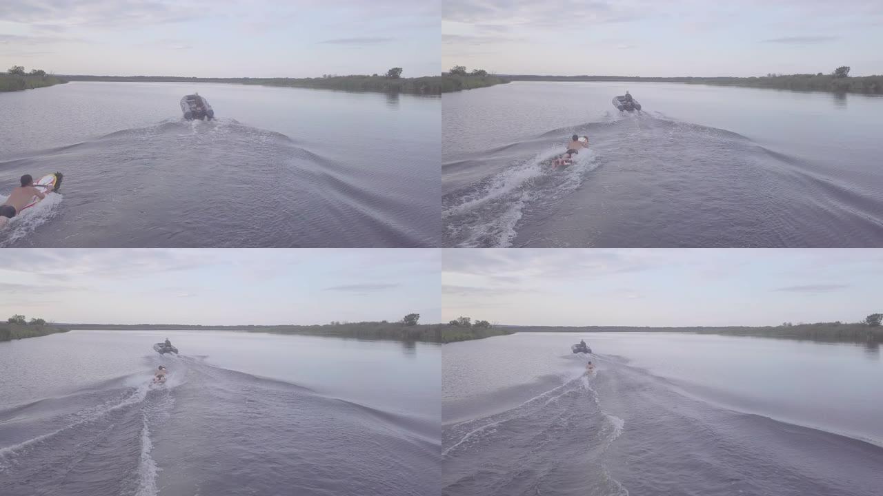 男子在平静平坦的湖面上的摩托艇后在冲浪板上滑行