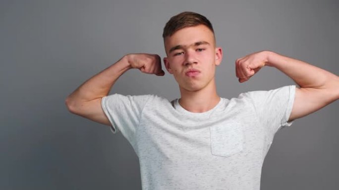 自信的运动少年男孩的肖像显示她的二头肌三头肌灰色背景提高了手臂的肌肉质量。运动员展示健身相机，乐于放
