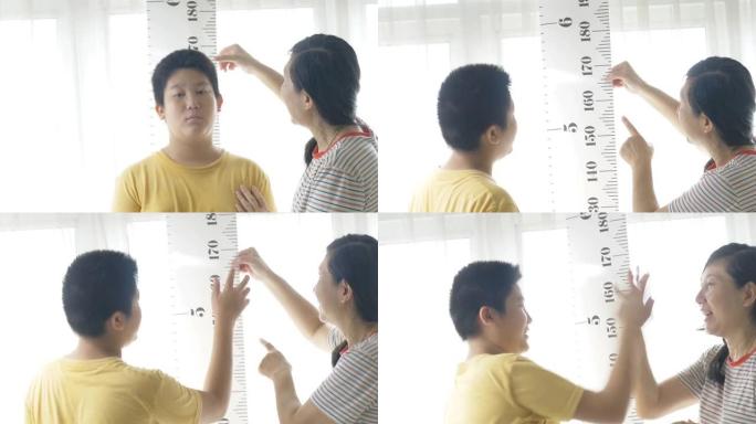 亚洲母亲对着窗户测量儿子的身高，生活方式的概念。