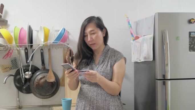 亚洲妇女使用信用卡在家里的厨房在线购物，生活方式的概念。