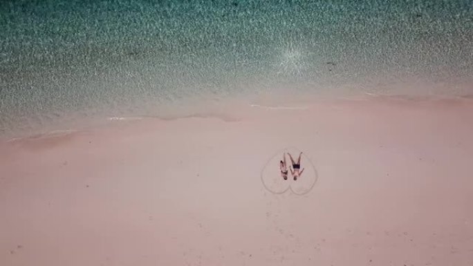 一架无人驾驶飞机拍摄的一对夫妇躺在粉红色的沙滩上，在印度尼西亚毛米尔附近的一个小岛上绘制的心脏上。快