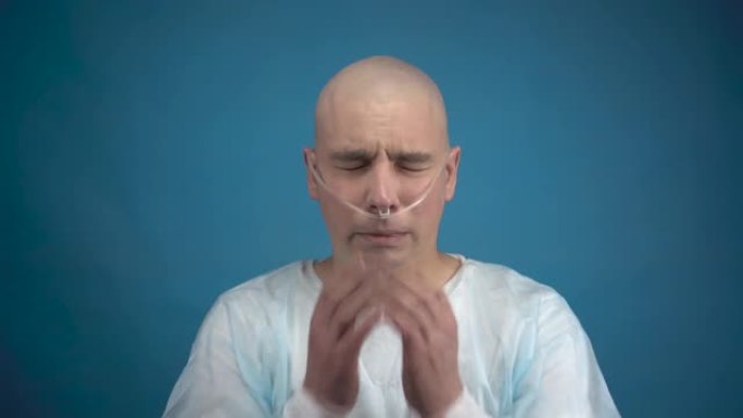 一个秃头的年轻人和肿瘤医生看着相机，在蓝色背景上哭泣。病人用手遮住脸。化疗导致脱发。