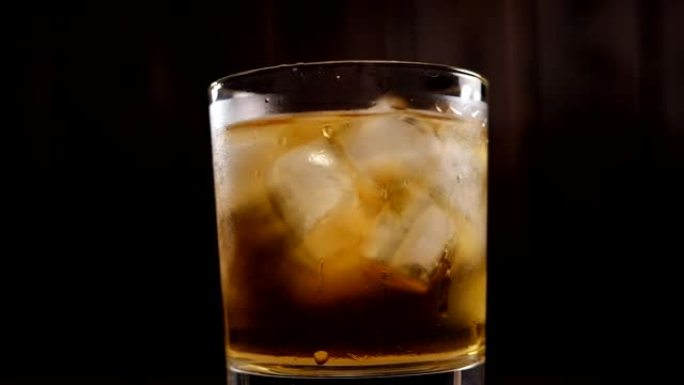 全杯威士忌加冰的特写镜头在黑色背景上缓慢旋转。
