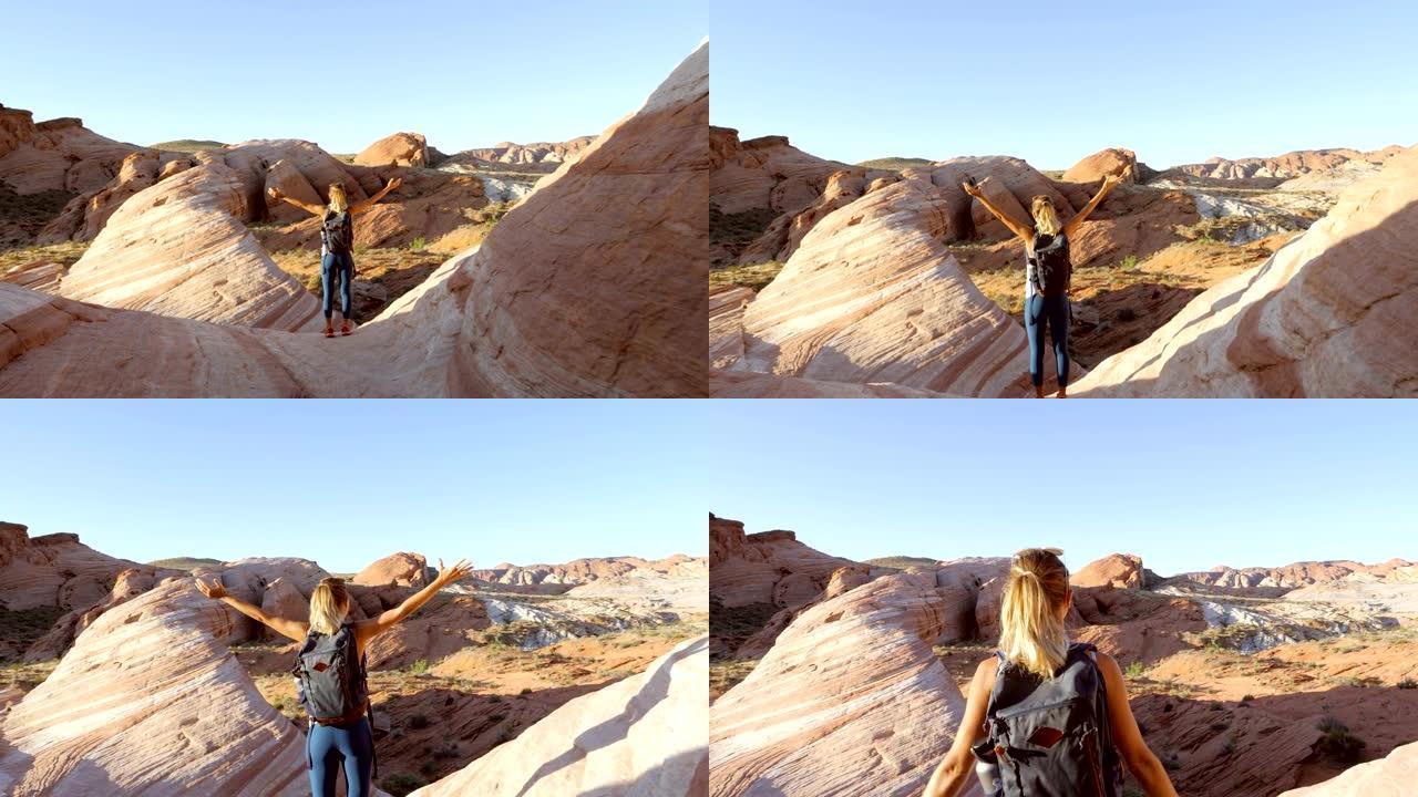 一名女性徒步旅行者在山顶上停下脚步，向外眺望岩石构成的圆顶。徒步旅行者张开双臂凝视自然景观