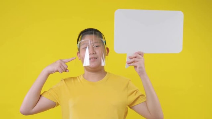 戴着面罩的亚洲青春期男孩在黄色背景上拿着空白的气泡。