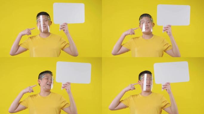 戴着面罩的亚洲青春期男孩在黄色背景上拿着空白的气泡。