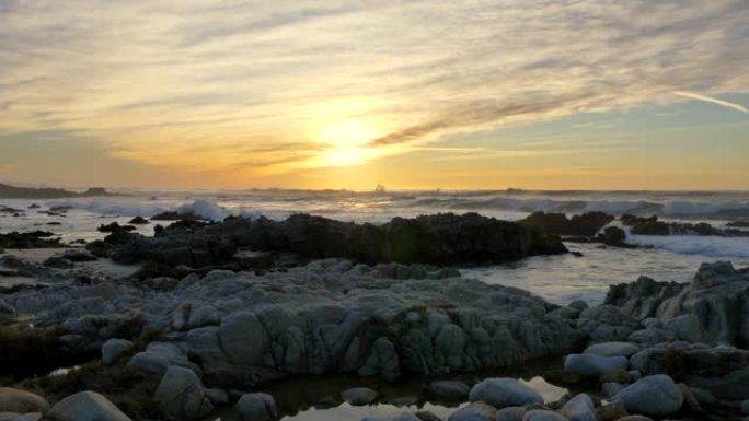 慢动作泛右太平洋海浪在暴风雨天气下在加利福尼亚州蒙特利半岛的太平洋格罗夫的日落天空下滚滚并在多岩石的