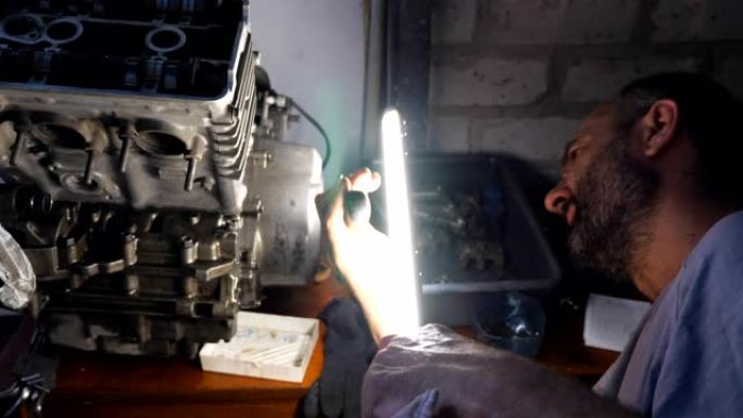 细心的机械师在车库或车间修理汽车发动机。男人在黑暗中使用明亮的手电筒工作。维修人员参与维修汽车。慢动