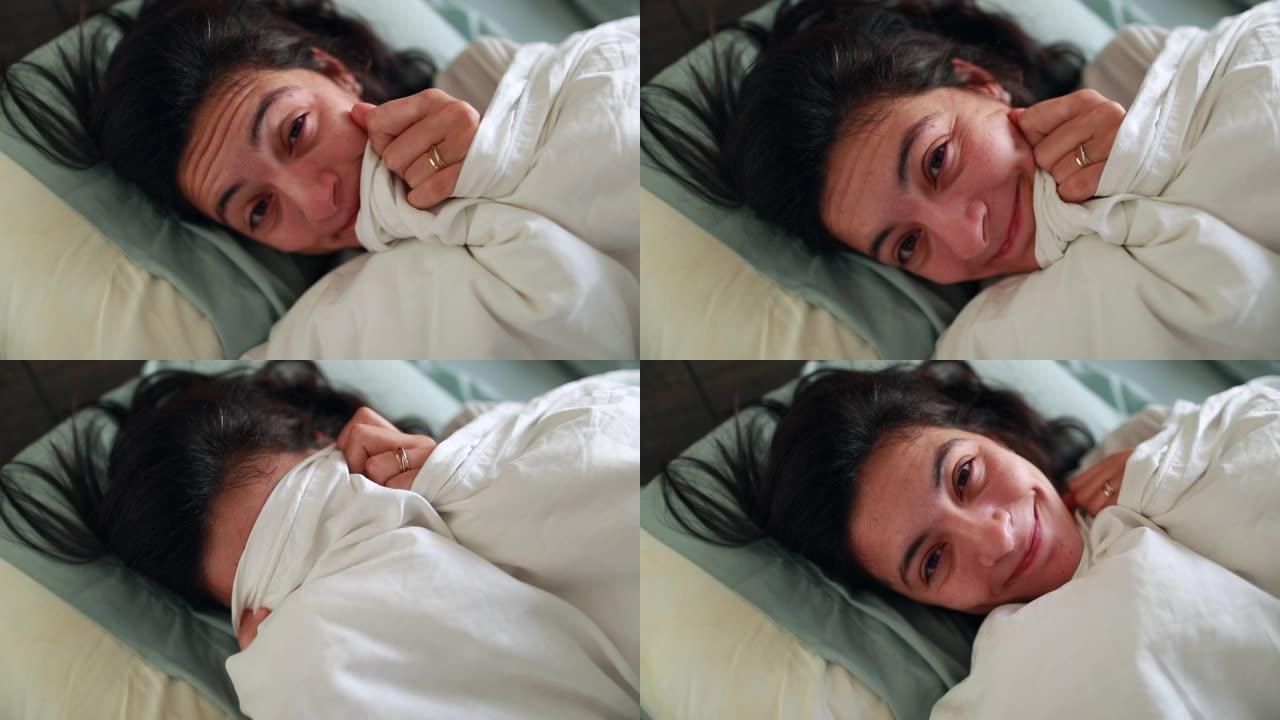 有趣的女人早上用床单玩躲猫猫，有趣的顽皮女孩在床上露出微笑的脸