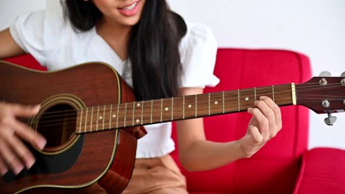 亚洲女人弹吉他，独自唱一首歌。新的正常生活方式和社交距离。在客厅放松和娱乐。