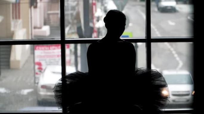 芭蕾舞演员的剪影在城市的背景下动人的舞蹈。穿着黑色短裙和尖头鞋。芭蕾舞中的黑天鹅形象。慢动作。