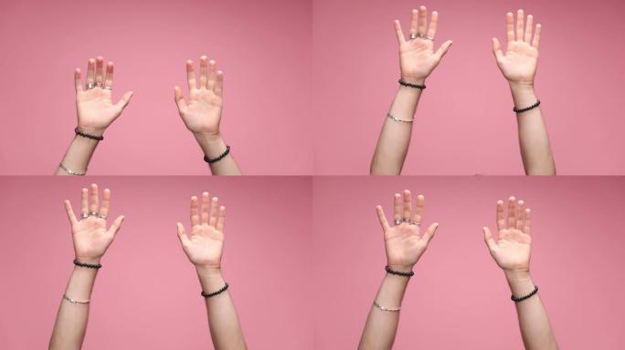 双手戴着手心张开的手镯和戒指开始指向相机，然后竖起大拇指，暗示您在粉红色背景下还可以