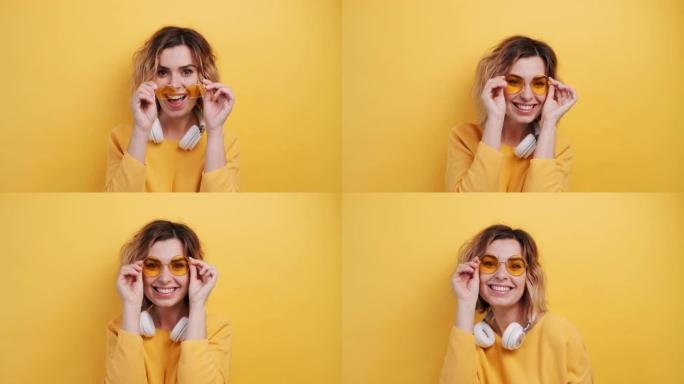 肖像快乐微笑的年轻性感女孩戴着白色耳机听音乐跳舞，在孤立的黄色背景上拉直黄色眼镜。乐事。人们的情感。