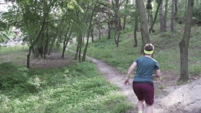 超重的女人在森林里跑步。肥胖女孩在公园里慢跑训练，坚持不懈地减肥。健身、减肥和健康生活的理念。越野越