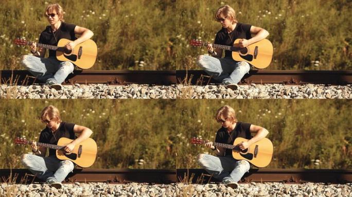 年轻的长发左撇子吉他手坐在铁路上用原声吉他弹奏歌曲