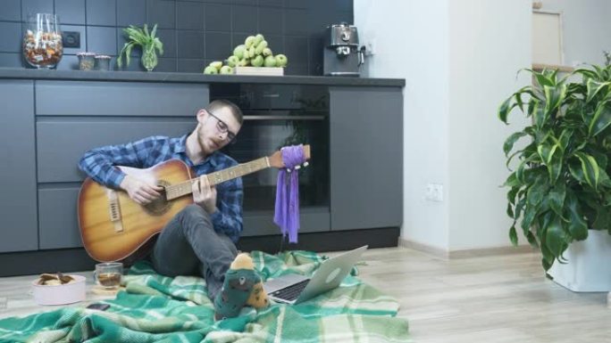 男人在舒适的公寓里坐在地板上弹奏原声吉他，唱着浪漫的抒情歌。男人在家弹吉他，在自我隔离和流行病检疫时