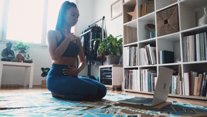女瑜伽教练在家里的笔记本电脑上领导冥想练习和呼吸练习