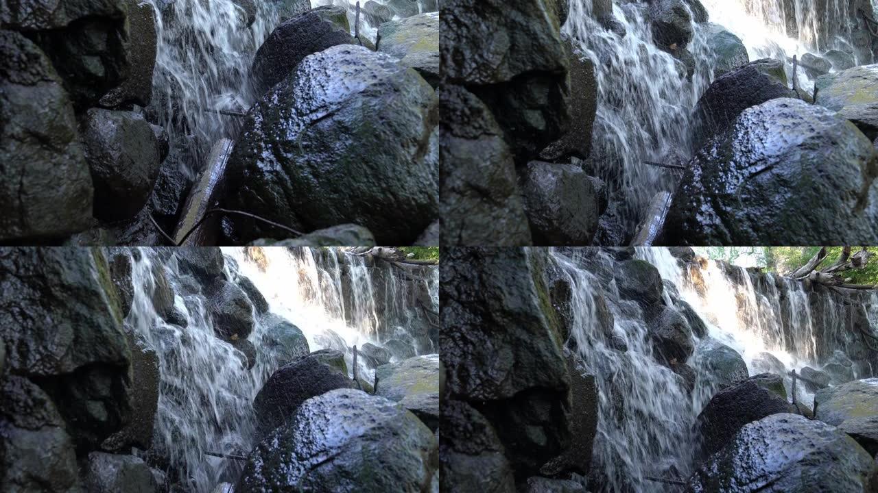 当水从岩石巨石表面向下倾泻并从瀑布下方的低处浸湿石头时，近距离平移瀑布的镜头。