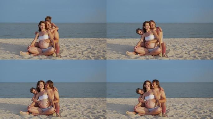 年轻的怀孕母亲与丈夫和她的小儿子在暑假的沙滩上玩耍和放松。怀孕，幸福的家庭，为人父母的观念。