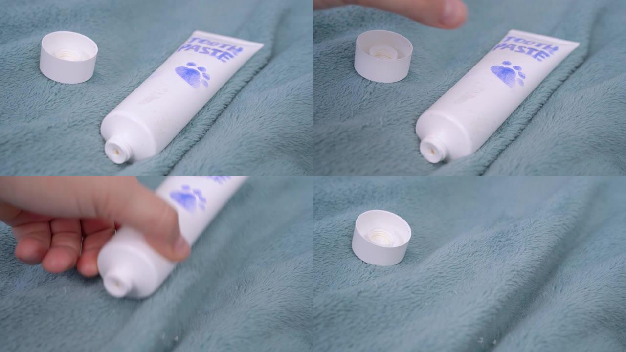 敞开的带宠物爪子的牙膏管放在温暖的毯子上，人的手用糊剂刷狗或猫的牙齿，关闭。日常口腔卫生设备。