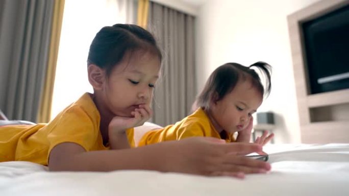 亚洲小宝宝用手机和小妹妹在卧室里晒太阳