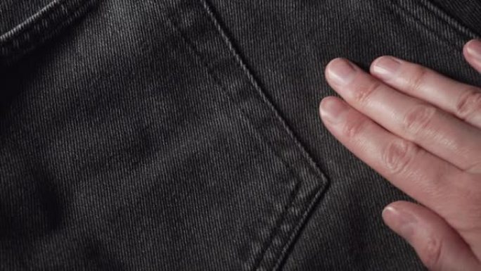 女孩摸着一条光滑的黑色牛仔裤，在服装店或纺织厂检查布料的质量
