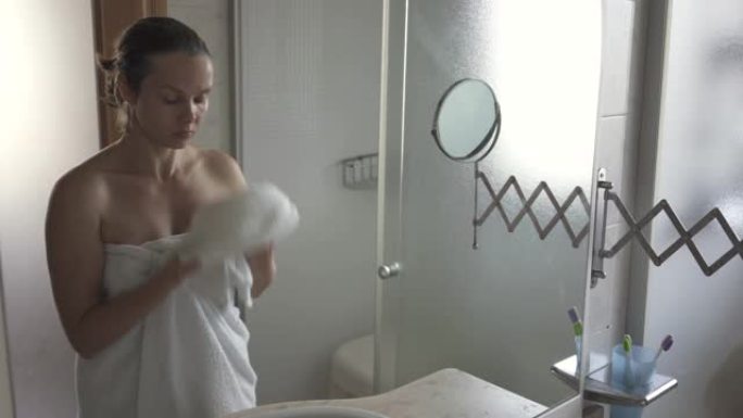 女人看着镜子洗完后用毛巾擦干脸