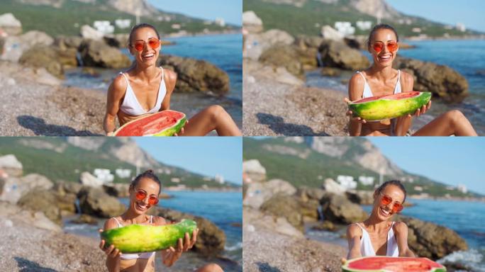 穿着比基尼的快乐女孩拿着大片西瓜坐在海边的沙滩上