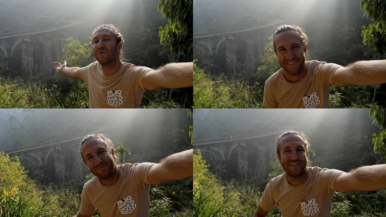 斯里兰卡快乐旅行男人的自拍视频，展示了古老的火车拱桥和茶园小山的美丽位置。男子视频聊天在线交流分享冒