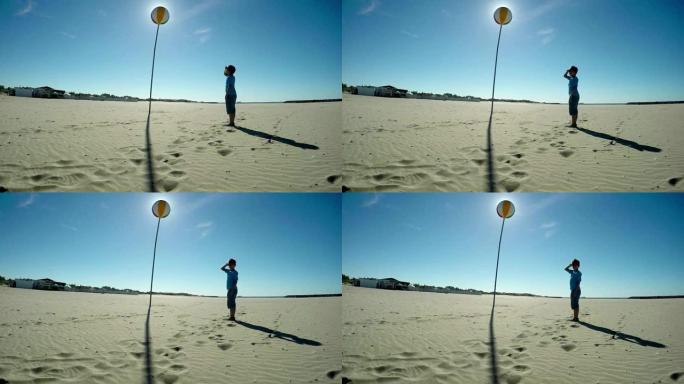 一个小男孩在海滩上看着天气球的剪影