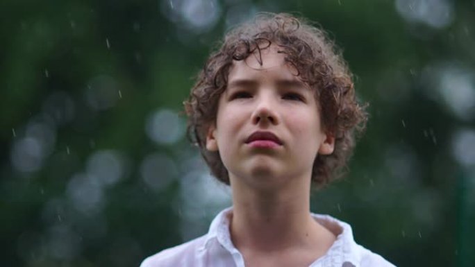 一个悲伤的卷发少年的亲密肖像站在倾盆大雨中。青春期概念的心理问题