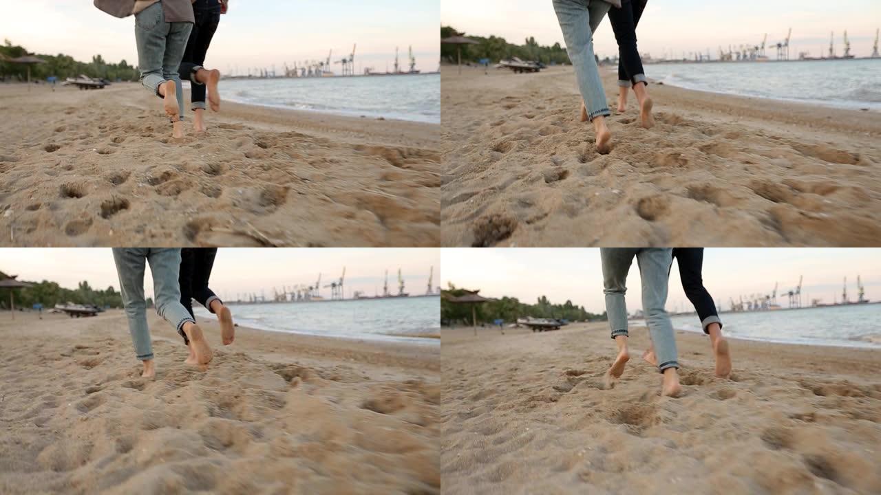 在海边的海滩上慢动作，浪漫的情侣脚在沙滩上奔跑，向后低角度的视图。男朋友和女朋友在海边玩得开心。恋爱