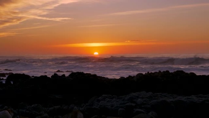 慢动作太平洋海浪在暴风雨天气下在加利福尼亚州蒙特利半岛的太平洋格罗夫的日落天空下滚滚并在多岩石的海岸