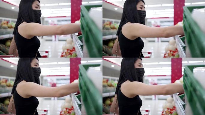 独立的亚洲妇女戴着口罩选择货架上的商品，站在超市货架前看零售超市内的产品，新冠肺炎大流行，选择食品