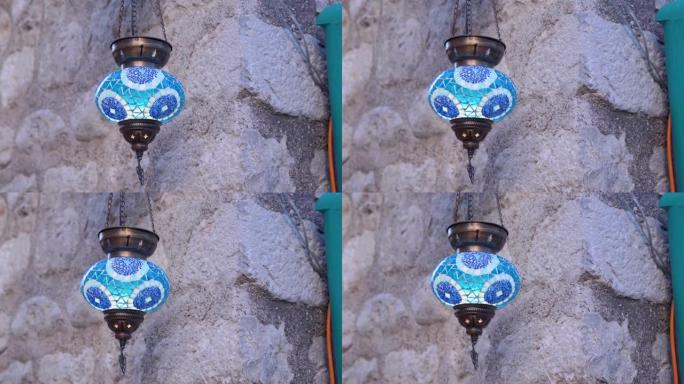 美丽的传统东方蓝色灯笼在风中在坚挺的石墙上闪烁。市场上手工灯光的多彩背景。
