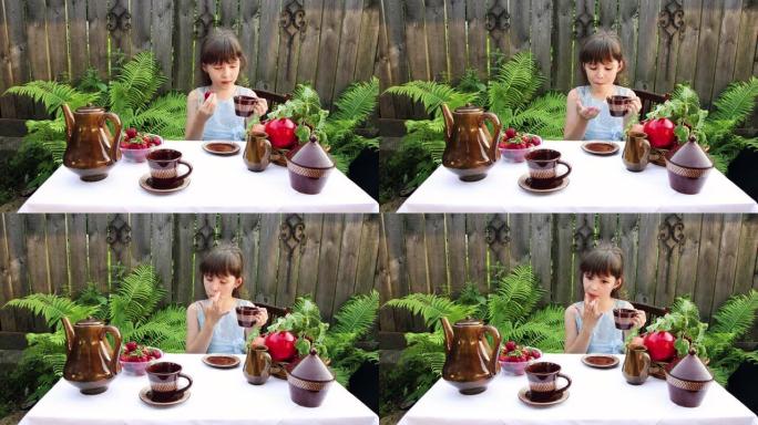 一个小女孩喝茶，吃浆果，舔手指。