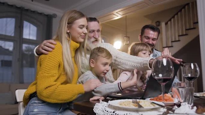迷人的成人和儿童家庭坐在桌旁，在视频通话中与计算机对话者道别