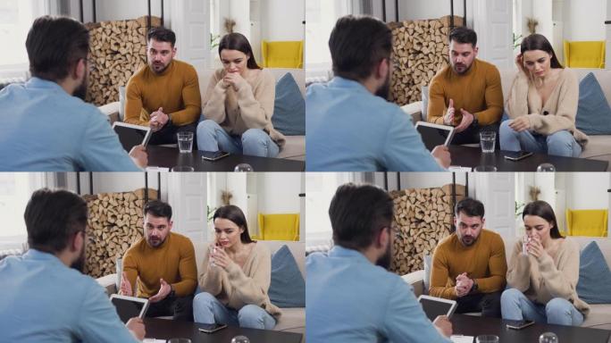 好看的不快乐的现代年轻已婚夫妇坐在沙发上进行心理学家访问，并寻求帮助以了解他们在人际关系中的不和谐