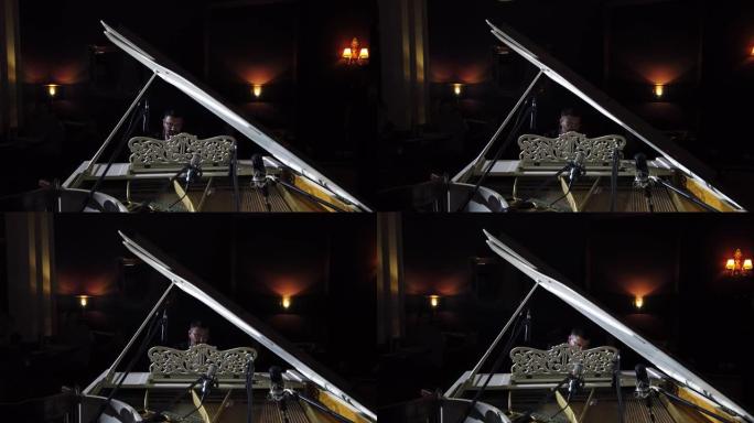 钢琴家在观众背景下表演自己的音乐的镜头。透过三角钢琴观看。