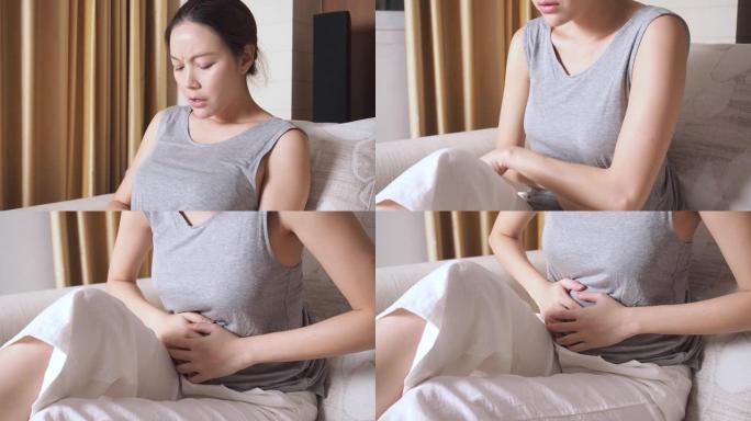 坐在客厅沙发上的亚洲女人胃痛。女性因怀孕而腹痛。