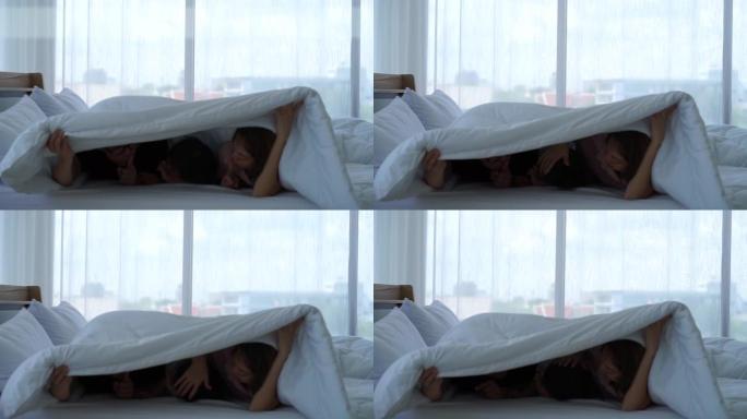 亚洲自闭症障碍小女孩和父母在白色床上玩耍，躲在房子里的白色毯子下