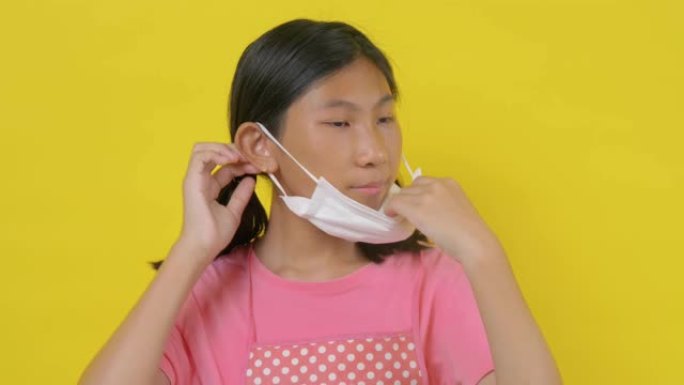 竖起大拇指的亚洲女孩戴着黄色背景的白色面具，新型冠状病毒肺炎概念。
