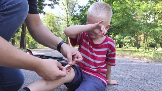 一个四岁男孩从踏板车上摔下来，摔断了膝盖。爸爸通过消毒伤口和涂抹石膏来提供急救。