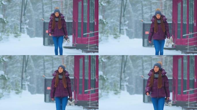 穿着紫色夹克的女人在白雪皑皑的公园里拿着溜冰鞋散步