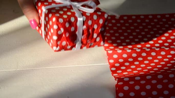 包装节日礼物，俯视图。一个不认识的女人用剪子剪的丝带和红色的包装纸包装礼品盒