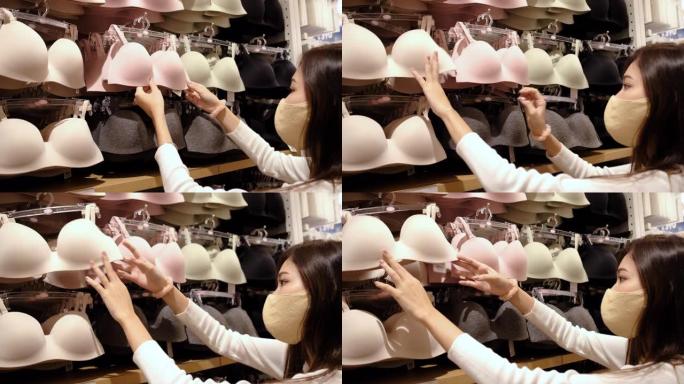 冠状病毒大流行结束后，戴着口罩和新的正常生活方式的年轻亚洲女性在百货商店、购物中心选择胸罩并重新开店