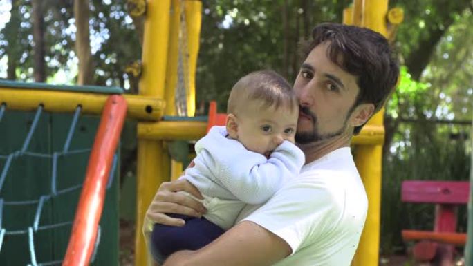 爸爸在户外游乐场公园抱着宝贝儿子，热爱真实的关系