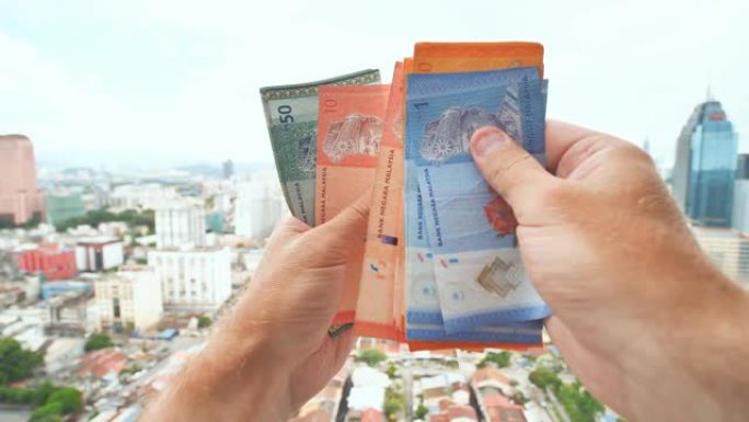 一名年轻人在吉隆坡市中心的背景下用手讲述马来西亚的钱