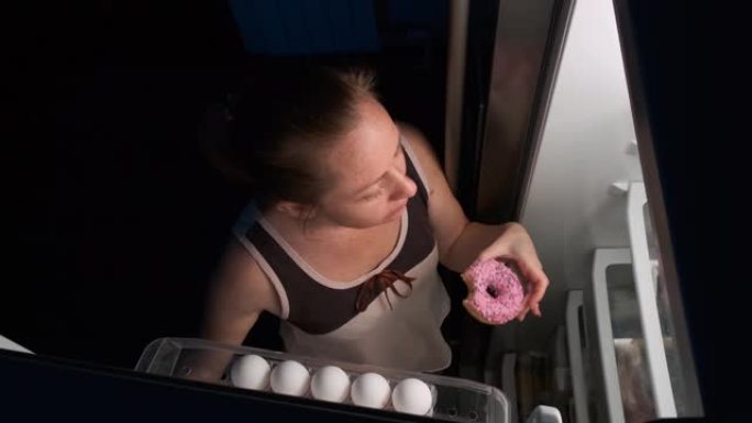 女人晚上从冰箱里拿走甜甜圈